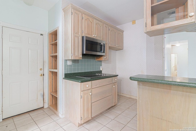 kitchen featuring stainless steel microwave, dark countertops, light tile patterned floors, black electric cooktop, and backsplash
