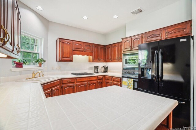 kitchen with black appliances, a sink, tile countertops, recessed lighting, and a peninsula