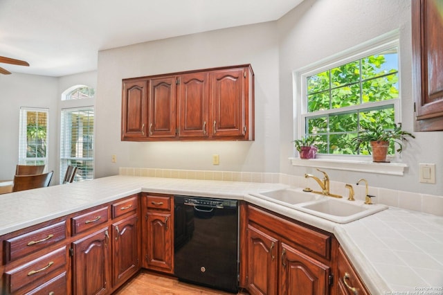 kitchen with black dishwasher, a sink, a ceiling fan, a peninsula, and tile counters