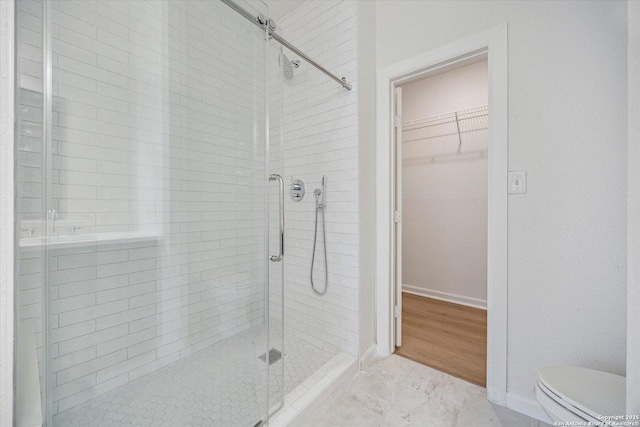 full bathroom with a shower stall, toilet, a walk in closet, and baseboards