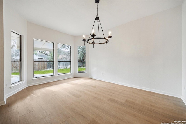 unfurnished dining area with a chandelier, light wood-type flooring, and baseboards