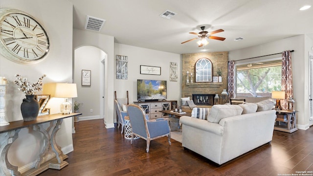 living room with a ceiling fan, arched walkways, a fireplace, dark wood finished floors, and baseboards