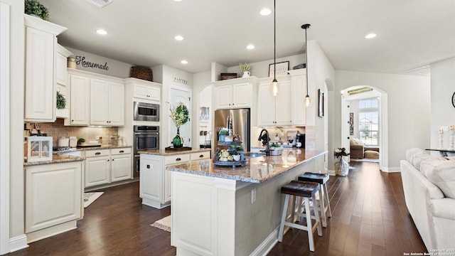 kitchen with appliances with stainless steel finishes, arched walkways, a sink, a center island, and decorative backsplash