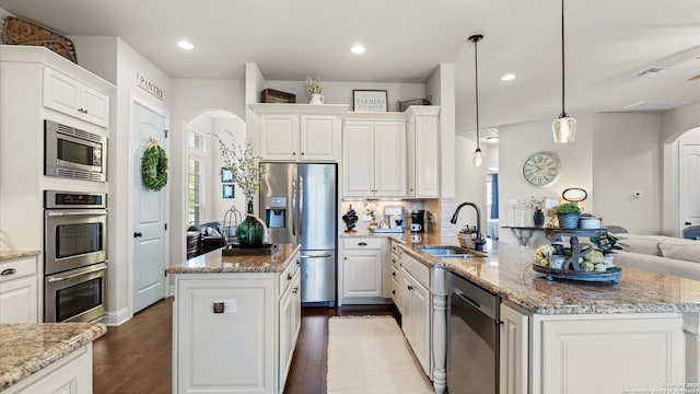 kitchen with appliances with stainless steel finishes, arched walkways, a sink, a center island, and white cabinetry