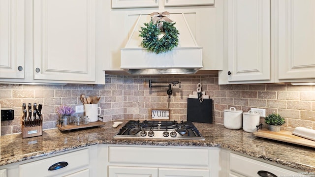 kitchen featuring stainless steel gas stovetop, white cabinetry, tasteful backsplash, premium range hood, and dark stone counters