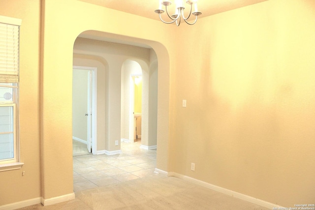 hall with arched walkways, a chandelier, light colored carpet, light tile patterned floors, and baseboards