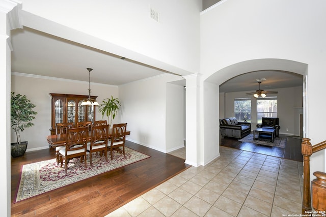 dining room with light wood-type flooring, ceiling fan, arched walkways, baseboards, and ornate columns