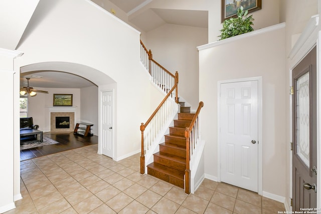 foyer with a high ceiling, light tile patterned floors, stairway, a fireplace, and a ceiling fan