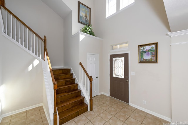 entryway with plenty of natural light, light tile patterned floors, stairway, and a towering ceiling