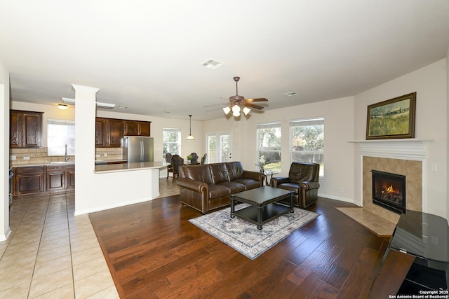 living area featuring ceiling fan, a tiled fireplace, plenty of natural light, and wood finished floors