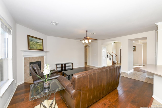 living area featuring dark wood-style floors, arched walkways, a fireplace, ceiling fan, and stairs