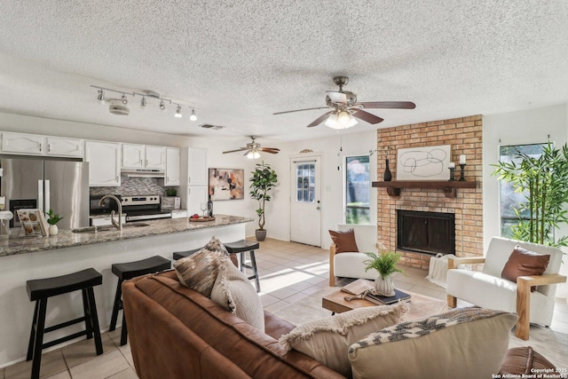 11731 Spring Rain, San Antonio, TX 78249 - living room featuring light tile patterned floors, a brick fireplace, a ceiling fan, and a textured ceiling