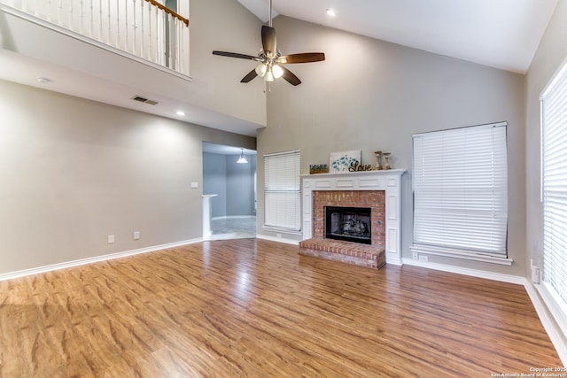 unfurnished living room featuring ceiling fan, wood finished floors, high vaulted ceiling, a brick fireplace, and baseboards