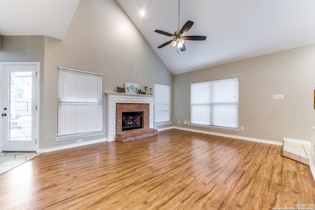 unfurnished living room with high vaulted ceiling, light wood finished floors, a ceiling fan, baseboards, and a fireplace