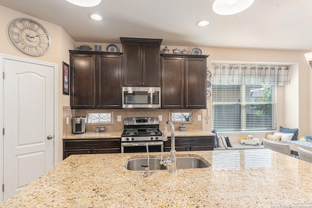 12338 Belfort Pt, Schertz, TX 78154 - kitchen with appliances with stainless steel finishes, a sink, dark brown cabinets, tasteful backsplash, and light stone countertops