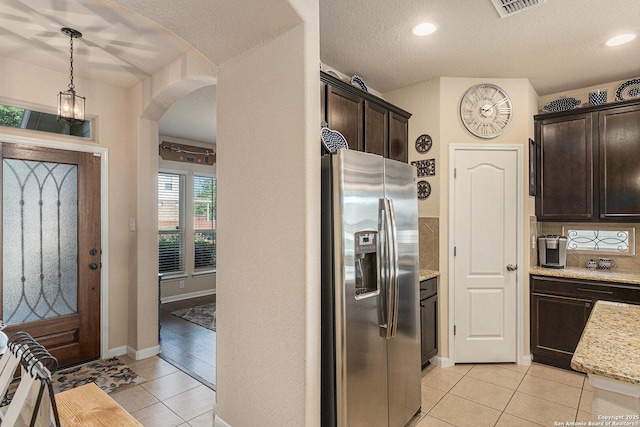 12338 Belfort Pt, Schertz, TX 78154 - kitchen featuring stainless steel fridge, light tile patterned floors, dark brown cabinets, arched walkways, and light stone countertops