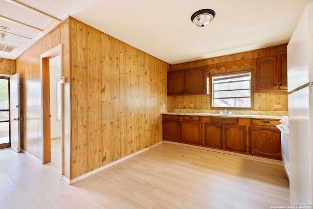 kitchen with wooden walls, light countertops, plenty of natural light, brown cabinetry, and a sink