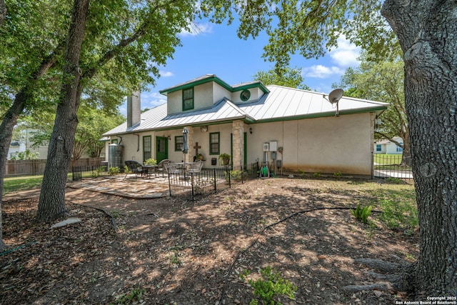 107 River Knl, Castroville, TX 78009 - back of house featuring a standing seam roof, stucco siding, metal roof, fence, and a chimney