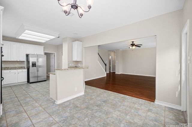 18127 Brookwood Frst, San Antonio, TX 78258 - kitchen with stainless steel fridge, white cabinets, light stone counters, a chandelier, and a peninsula