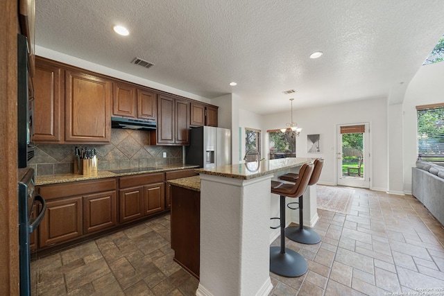 1326 Walkers Way, San Antonio, TX 78216 - kitchen with fridge with ice dispenser, under cabinet range hood, black electric stovetop, stone tile flooring, and a textured ceiling