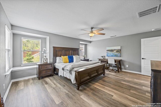 11334 Hill Top Bnd, Helotes, TX 78023 - bedroom featuring wood finished floors, multiple windows, baseboards, a textured ceiling, and ceiling fan
