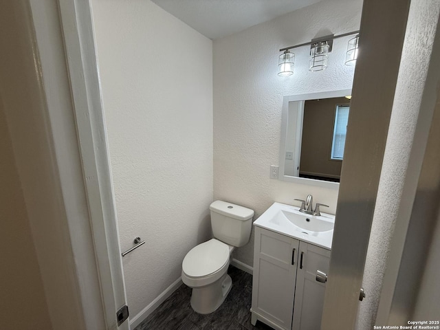 bathroom with vanity, toilet, baseboards, and a textured wall