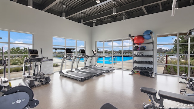 gym with a towering ceiling, plenty of natural light, and beam ceiling