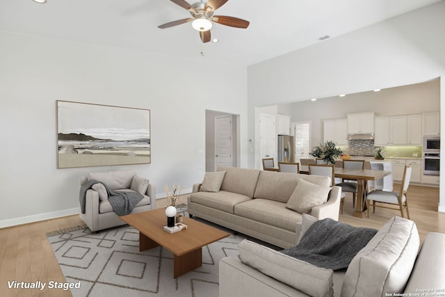 living room with ceiling fan, recessed lighting, light wood-type flooring, baseboards, and a high ceiling