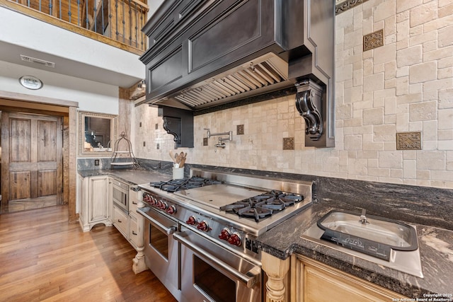 kitchen featuring range with two ovens, built in microwave, decorative backsplash, light wood-type flooring, and dark stone countertops