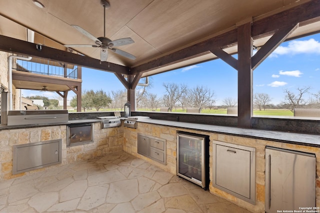 view of patio / terrace featuring beverage cooler, ceiling fan, an outdoor kitchen, and a grill