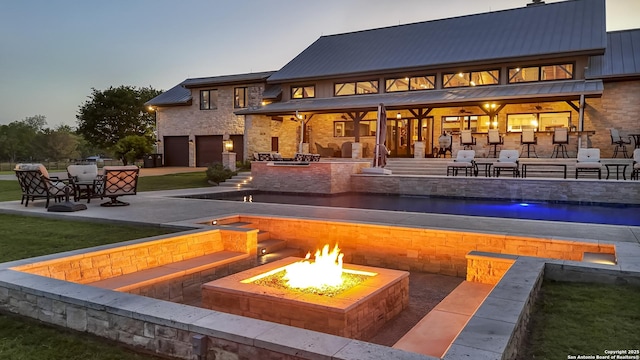 back of property at dusk with an outdoor fire pit, a bar, a standing seam roof, metal roof, and a garage