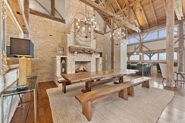 dining room with high vaulted ceiling, hardwood / wood-style flooring, a chandelier, beamed ceiling, and a fireplace