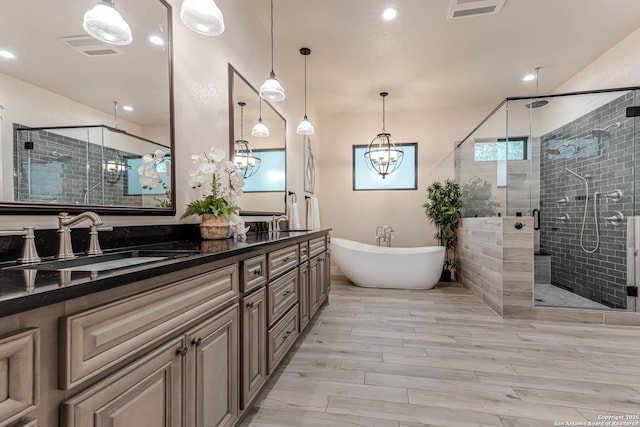bathroom featuring a shower stall, a freestanding tub, a chandelier, double vanity, and wood finished floors