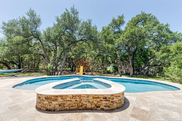 view of pool with view of scattered trees, a patio, a playground, and a pool with connected hot tub