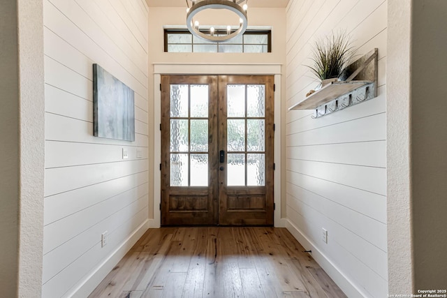 doorway to outside with french doors, wood walls, hardwood / wood-style floors, healthy amount of natural light, and a chandelier