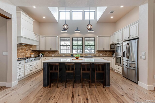 kitchen with stainless steel appliances, white cabinets, a kitchen breakfast bar, light wood-type flooring, and a center island