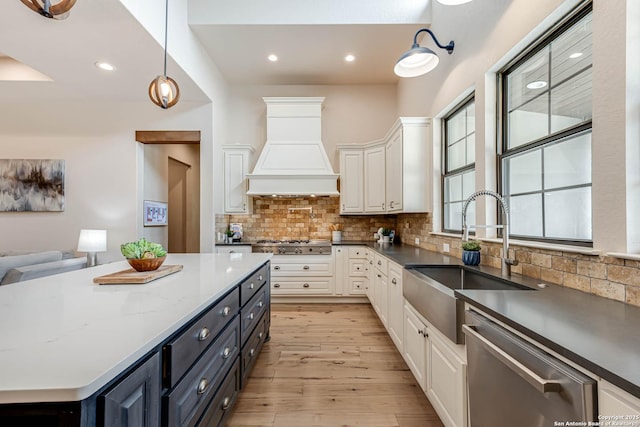 kitchen with stainless steel appliances, custom exhaust hood, a sink, white cabinetry, and backsplash