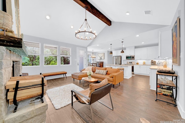 living room with a chandelier, beam ceiling, light wood-style flooring, a stone fireplace, and recessed lighting