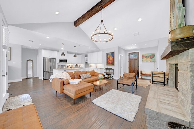 living area featuring a chandelier, beamed ceiling, wood finished floors, recessed lighting, and a stone fireplace
