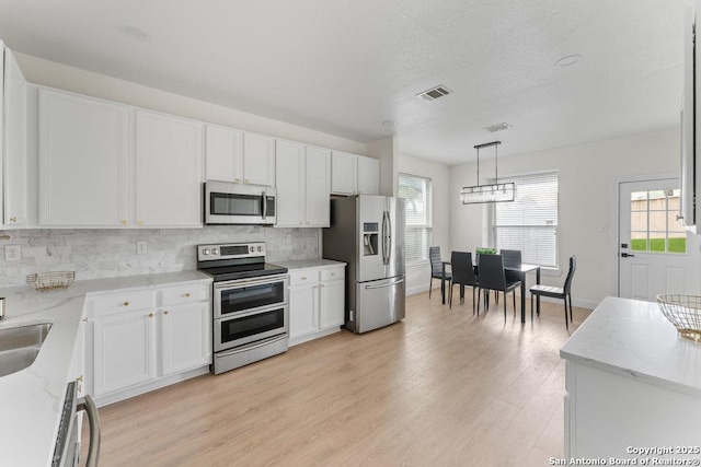 8651 Eagle Peak, Helotes, TX 78023 - kitchen with appliances with stainless steel finishes, tasteful backsplash, white cabinets, light wood-style floors, and plenty of natural light