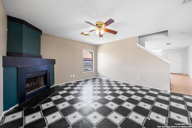unfurnished living room with a ceiling fan, a fireplace, a textured ceiling, and baseboards