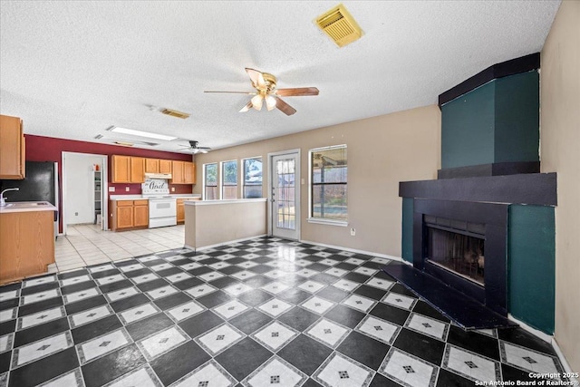 unfurnished living room with a ceiling fan, a textured ceiling, a large fireplace, baseboards, and a sink