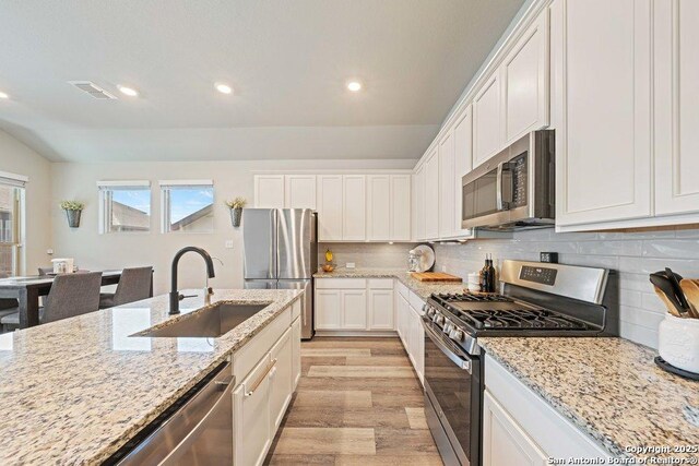 kitchen with stainless steel appliances, a sink, light wood-style floors, recessed lighting, and white cabinetry