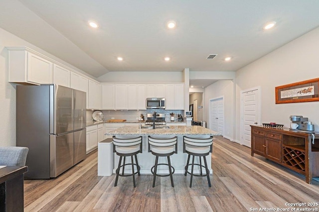 kitchen featuring appliances with stainless steel finishes, white cabinetry, decorative backsplash, light stone counters, and a breakfast bar