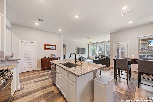 kitchen featuring a sink, appliances with stainless steel finishes, open floor plan, a ceiling fan, and light wood finished floors