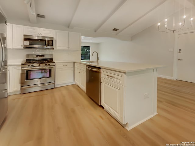 kitchen featuring appliances with stainless steel finishes, a peninsula, light wood-style flooring, a sink, and light countertops