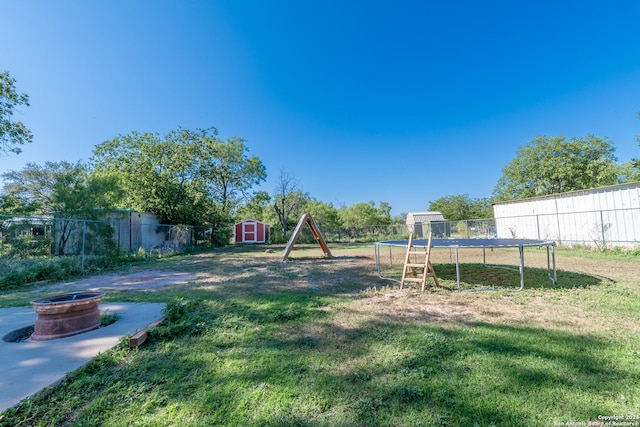 view of yard featuring a trampoline, a shed, an outdoor structure, and a fire pit
