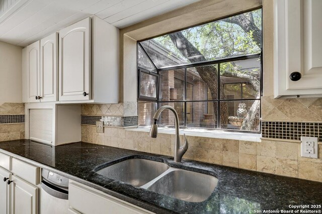kitchen with a sink, white cabinetry, decorative backsplash, and dark stone counters