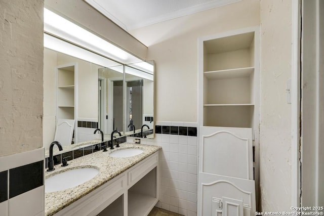 full bath with tile walls, a wainscoted wall, double vanity, and crown molding