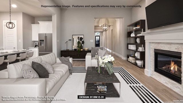 living room featuring light wood-style flooring, a chandelier, a glass covered fireplace, and baseboards